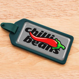 A rectangular resin-coated label in grey and green featuring a red chili pepper and text. A rectangular resin-coated label in grey and green featuring a red chili pepper and text.