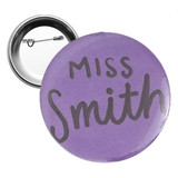 A round 58mm button badge in purple with a silver backing and a pin mechanism.
