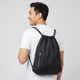 A man wearing a black drawstring bag with a logo on the back, featuring adjustable straps and a front zip pocket.