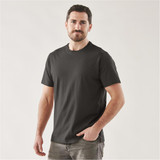 A man wearing a black short sleeve t-shirt, standing confidently with one hand in his pocket. The shirt has a logo.