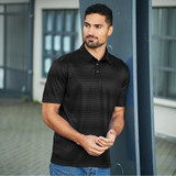 A man wearing a black polo shirt stands outdoors next to a pillar. The shirt features a subtle pattern and a logo.