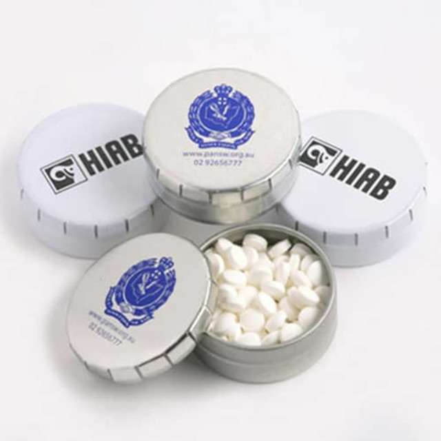 A silver tin with a removable lid filled with white tablets, surrounded by similar tins featuring logos. A silver tin with a removable lid filled with white tablets, surrounded by similar tins featuring logos.