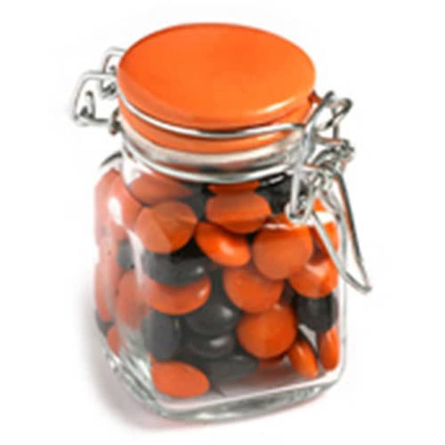 A glass clip lock jar filled with orange and black choc beans, featuring a branded sticker on the jar.