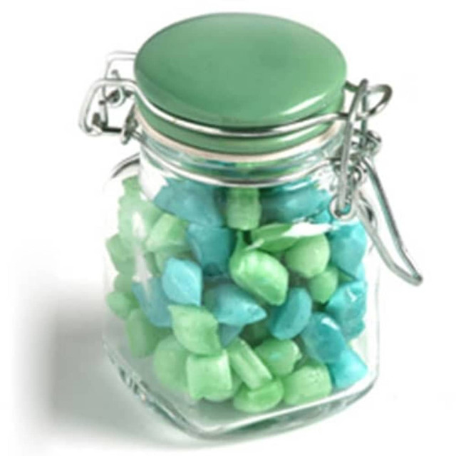 A glass clip lock jar filled with light green and blue humbug sweets, featuring a green lid and a metal clasp.