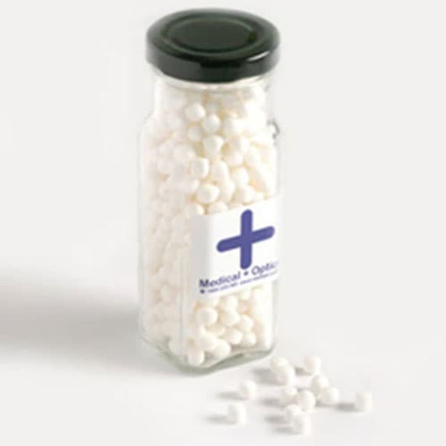 A tall glass jar filled with white mints, featuring a branded sticker and a black lid.