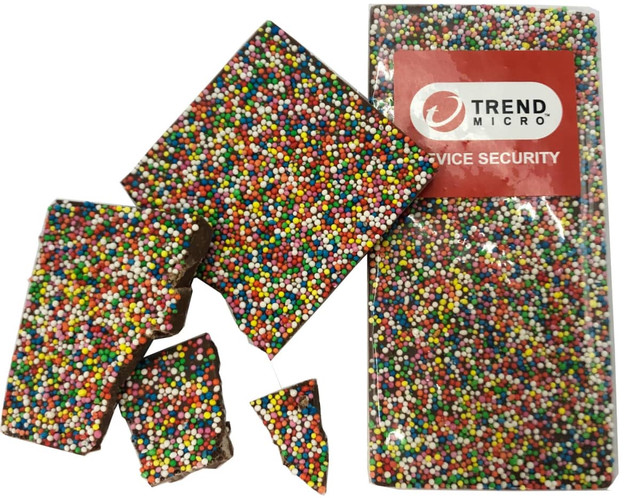 A milk chocolate bar covered in colourful 100s and 1000s, with several pieces broken off, and featuring a branding logo.