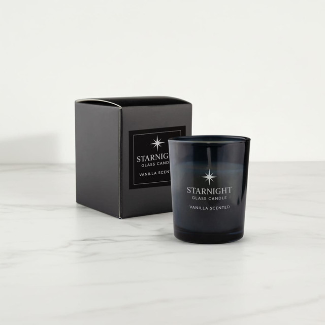 A black glass candle with a vanilla scent beside its black box packaging, set on a marble surface.