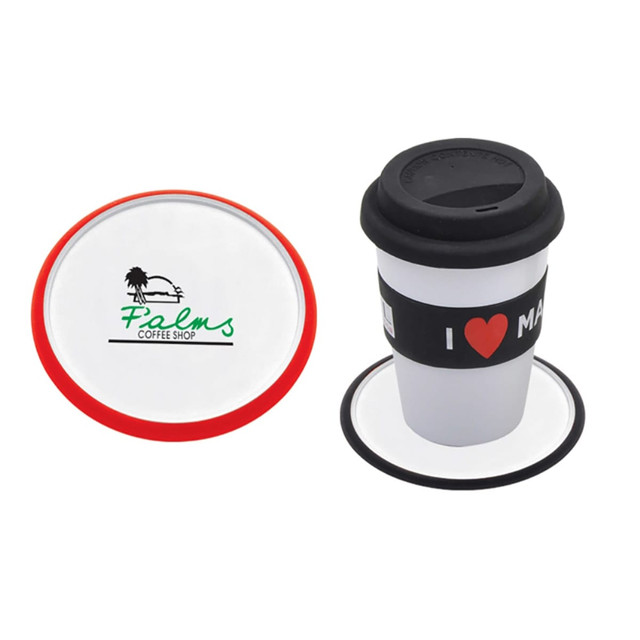 A red and white coaster with a logo, alongside a reusable coffee cup with a black lid and sleeve.