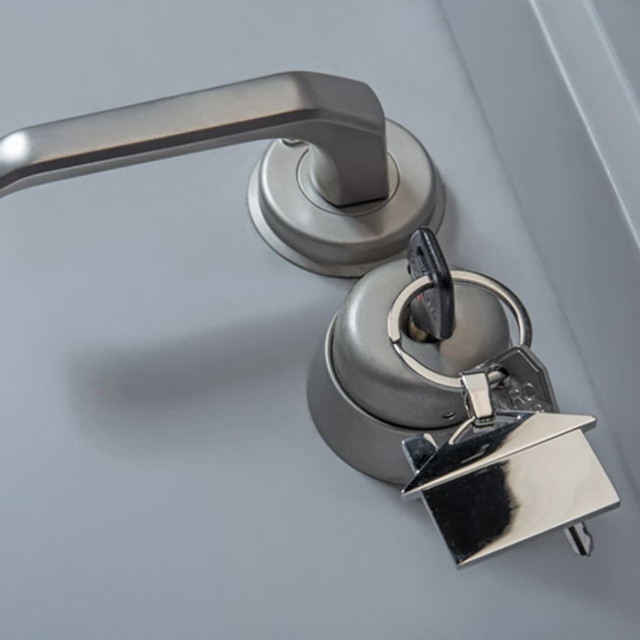 A silver house-shaped key ring attached to a silver door handle, set against a grey background.