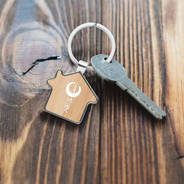 A bamboo house-shaped key ring in silver metal, paired with a standard key, resting on a wooden surface.