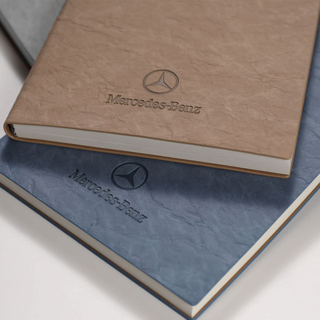 A brown and a blue notebook stacked, featuring a logo. Both have a textured cover and a simple design.