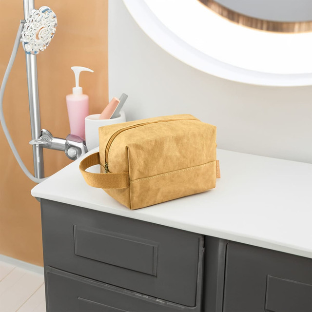 A yellow Kraft paper cosmetic bag with a zip closure, resting on a countertop. It has a handle and a logo.
