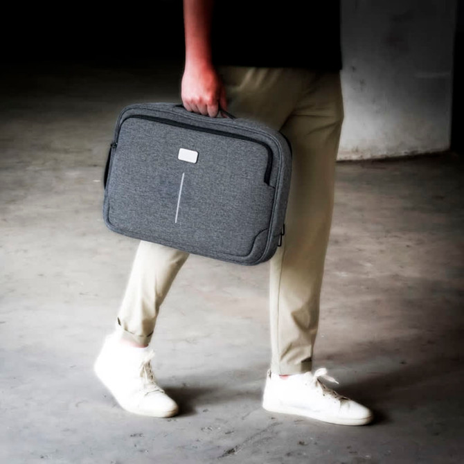 A grey laptop bag with a handle is being carried by a person in casual attire.