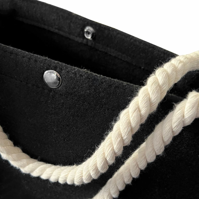 A black felt tote bag featuring a white rope handle and a snap closure at the top.