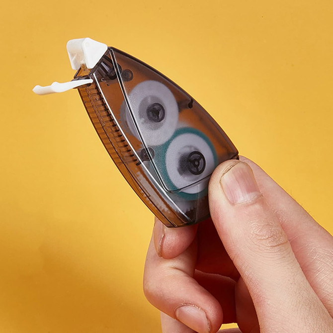 A hand holding a brown and transparent tape dispenser with a white tape inside, against a yellow background.