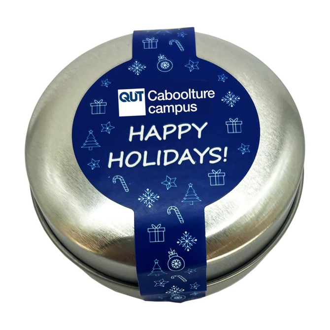 A round, silver candle tin featuring a blue label with festive designs and a holiday greeting.