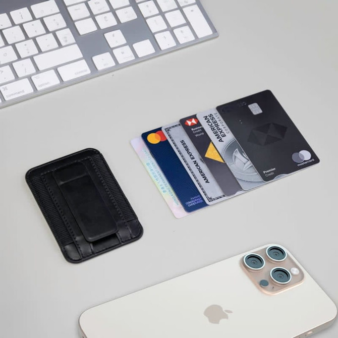 A black card holder with multiple credit cards beside a smartphone and a white keyboard on a light surface.