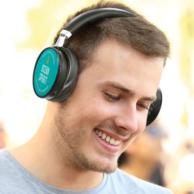 A pair of black noise-cancelling headphones worn by a smiling individual in a casual setting. Branding visible on the headphones.