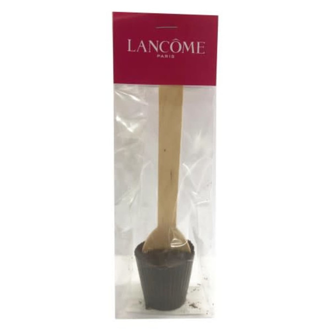 A chocolate spoon in a clear package, featuring a wooden stick and a brown chocolate base with a branding label at the top.