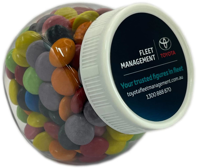 A clear plastic jar filled with colourful choc beans, featuring a branded lid and logo.