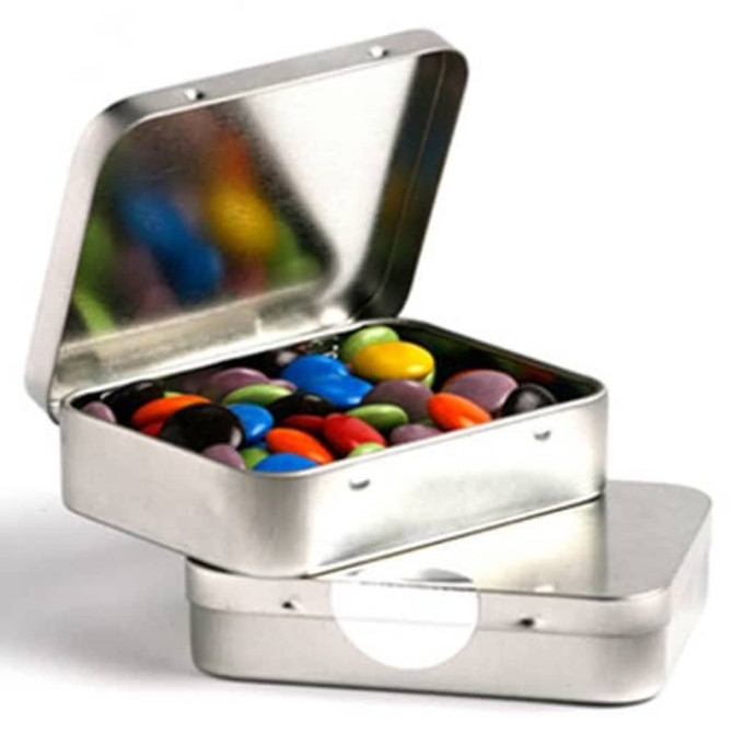 A rectangular silver tin filled with colourful chocolate beans, featuring a hinged lid. The tin has a branding logo.