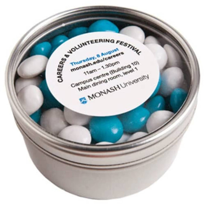 A round tin filled with chewy blue and white confectionery. The tin features a label with event details.