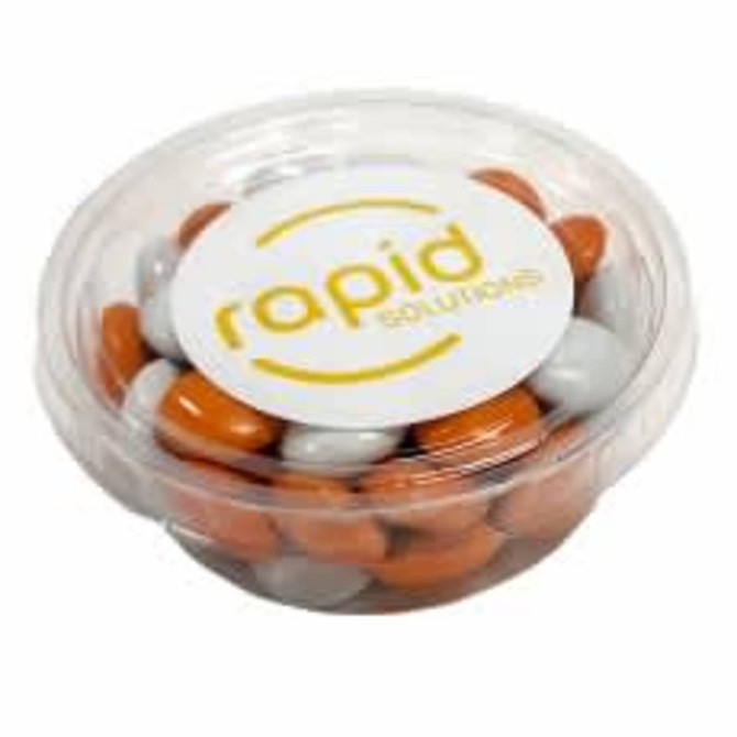 A clear tub containing orange and grey choc beans with a logo on the lid.