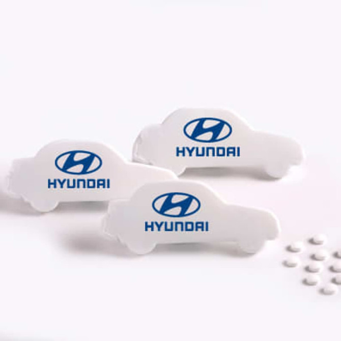 Three white car-shaped mint cards with a logo, accompanied by small white mint sweets scattered beside them.