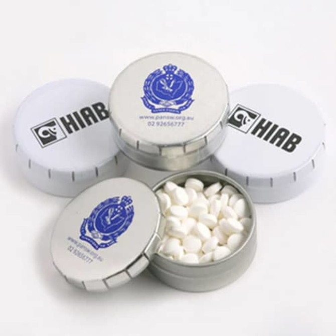 A tin container filled with white mints, featuring a silver finish and a logo on the lid.