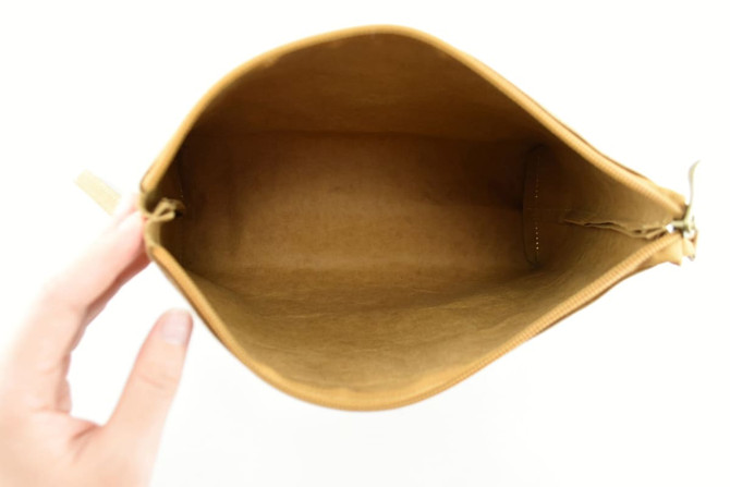 A hand holds a tan Kraft paper cosmetic bag, showcasing its spacious interior with no items inside.