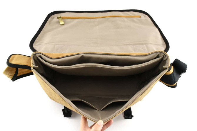 A tan kraft paper laptop messenger bag with a spacious interior and a zippered pocket, featuring a logo.