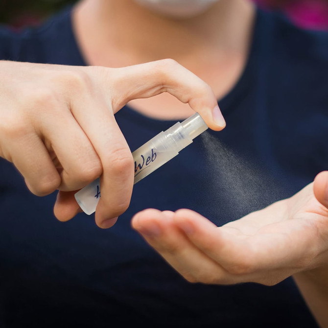 A clear mini hand sanitiser key ring being sprayed onto a palm, with a light mist visible.