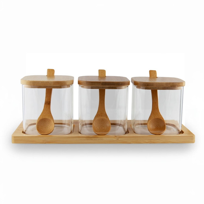 Three glass condiment jars with bamboo lids and wooden spoons, placed on a bamboo tray.