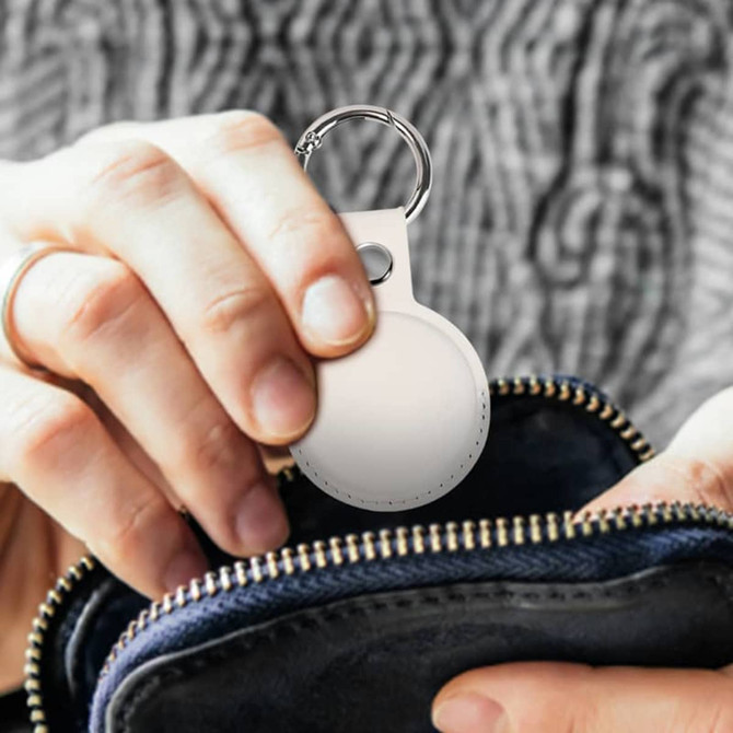 A white tracking tag is being placed into a navy blue pouch, held by a person with a knitted sweater.