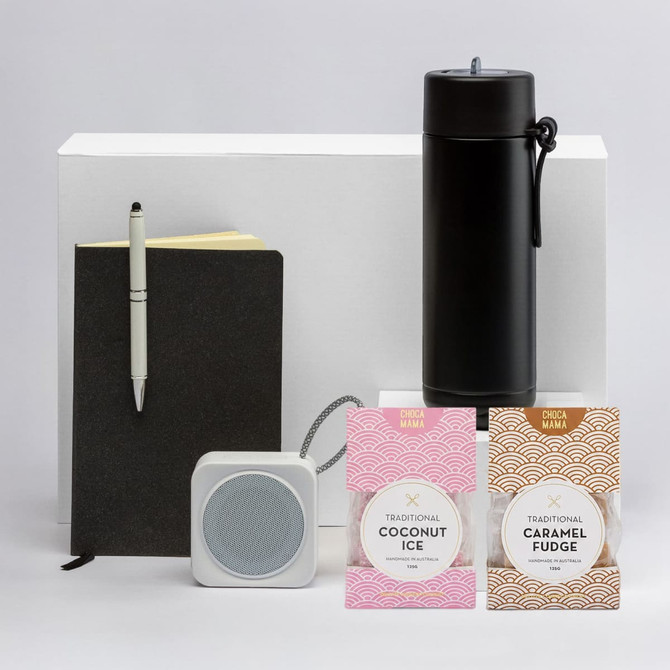 A black drink bottle, a notepad, a pen, a white speaker, and two packets of sweets in pink packaging.