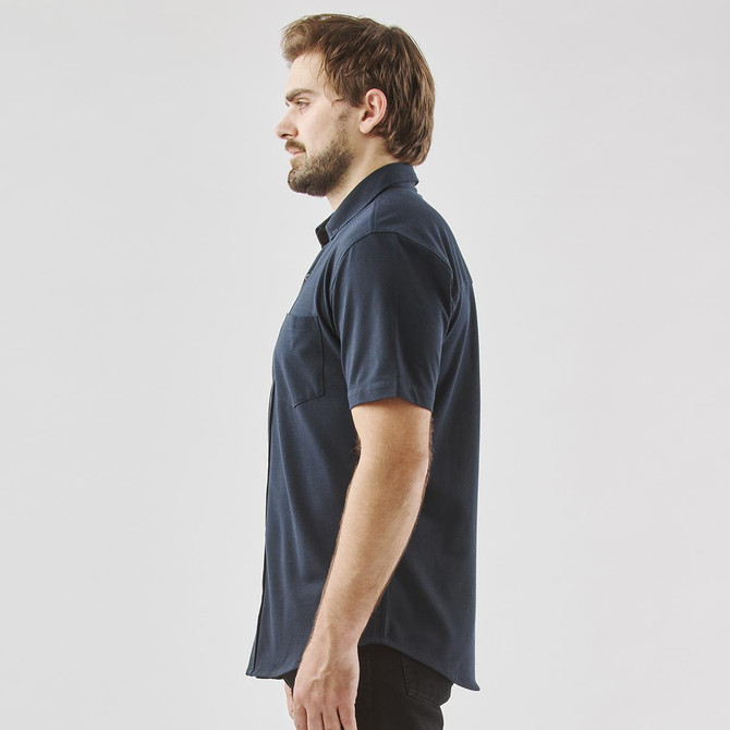 A dark navy short sleeve button-up shirt displayed on a model from the side, featuring a pocket and a logo.