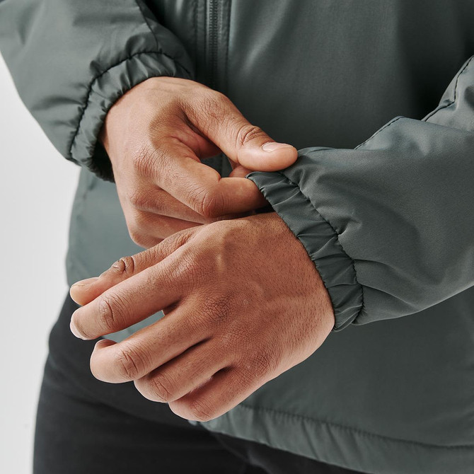 A close-up of hands adjusting the elastic cuff of a dark green thermal jacket, featuring a logo.