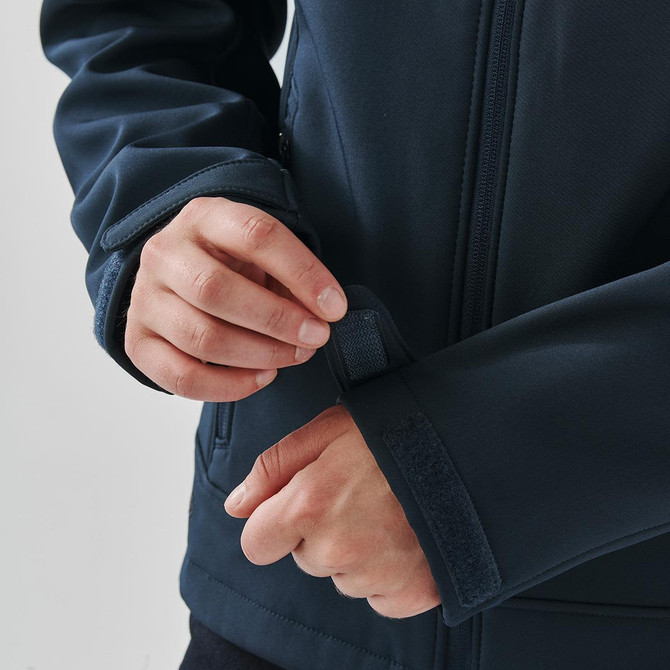 A dark blue softshell jacket with adjustable cuffs, featuring a person fastening the wrist strap.