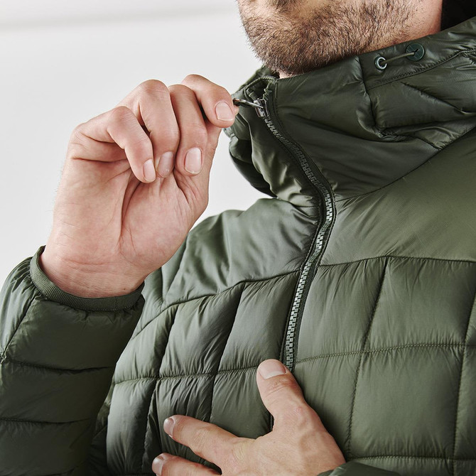 A close-up of a man adjusting the zipper on a dark green puffer jacket. The jacket features a high collar and quilted design.