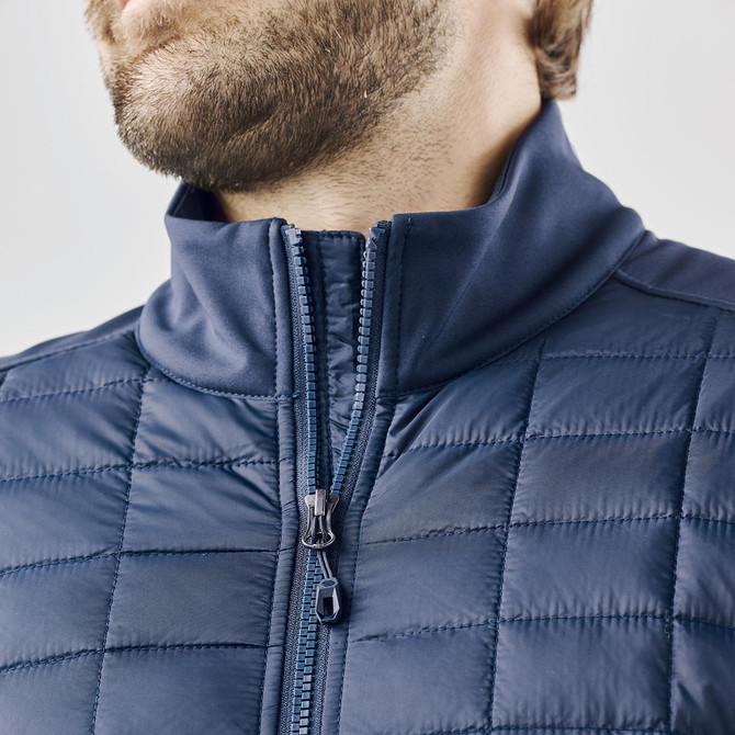 A men's softshell jacket in navy blue with a high collar and quilted texture. Features a zippered front.