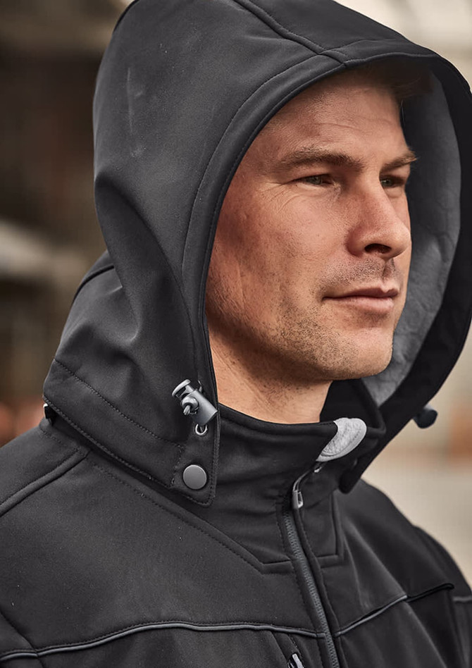 A man wearing a black unisex softshell jacket with a hood, featuring a branded logo on the chest.