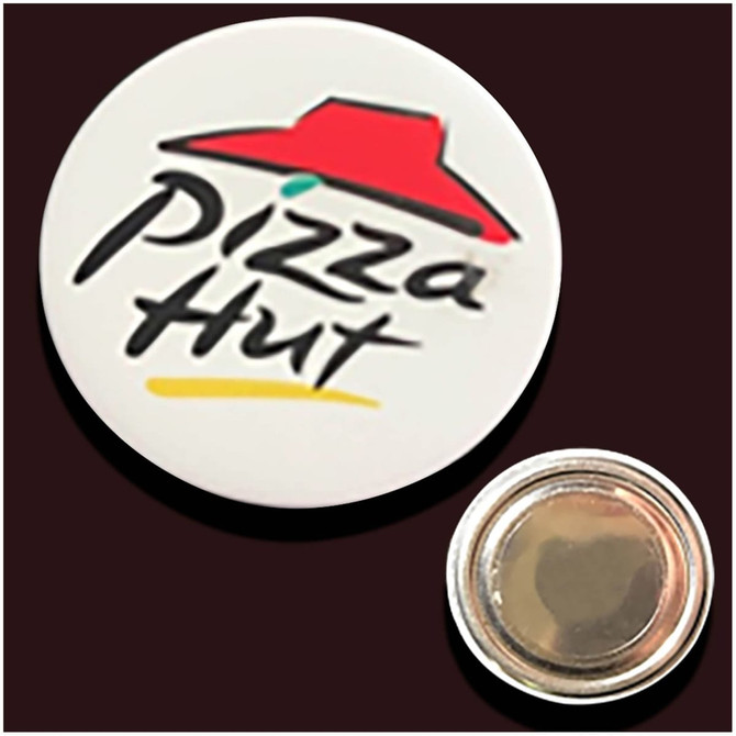 A round button badge featuring a logo with a red hat and black text on a white background. It has a metal backing.