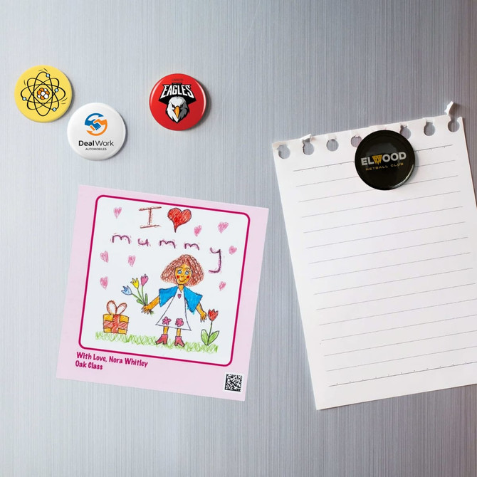 A collection of colourful button badges, including a drawing, displayed on a metallic surface with a notepad.