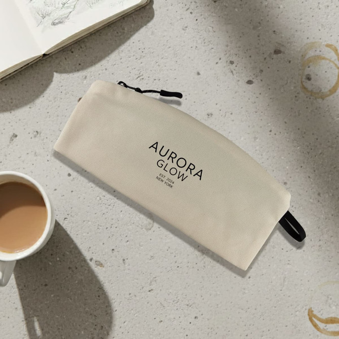 A medium cream cosmetic bag with a zip closure and a logo, placed beside a coffee cup and a notebook.