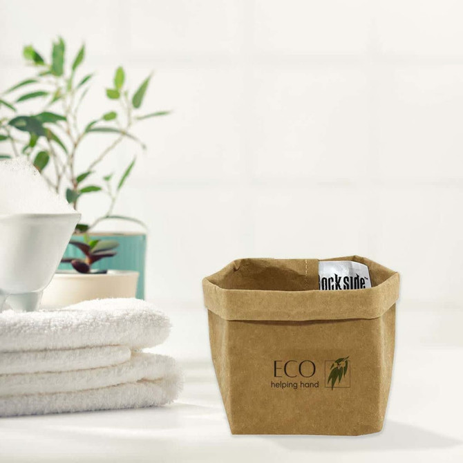 A small brown kraft paper storage bag with a logo, placed beside neatly folded white towels and a green plant.