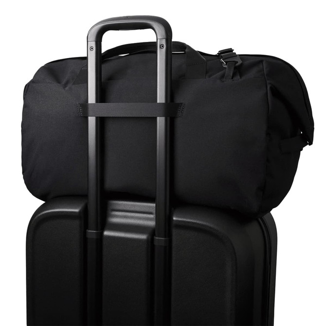 A black duffel bag sits on top of a black suitcase, featuring a trolley handle for easy transport.