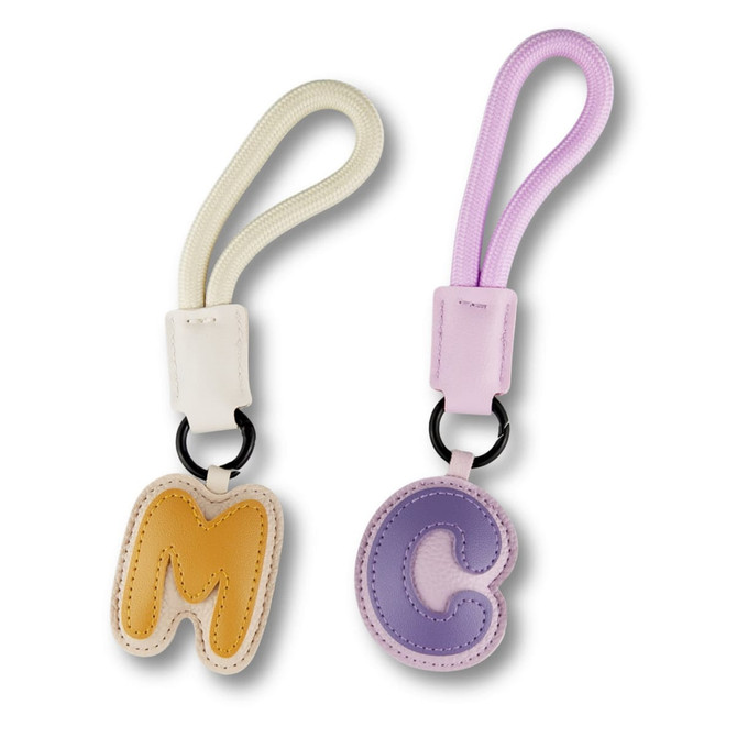 Two bag charms in pastel colours: one yellow 'M' and one purple 'C', each with a detachable strap.