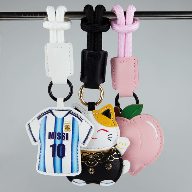 Three bag charms featuring a jersey, a cat, and a peach, in white, black, pink, and multicoloured designs.