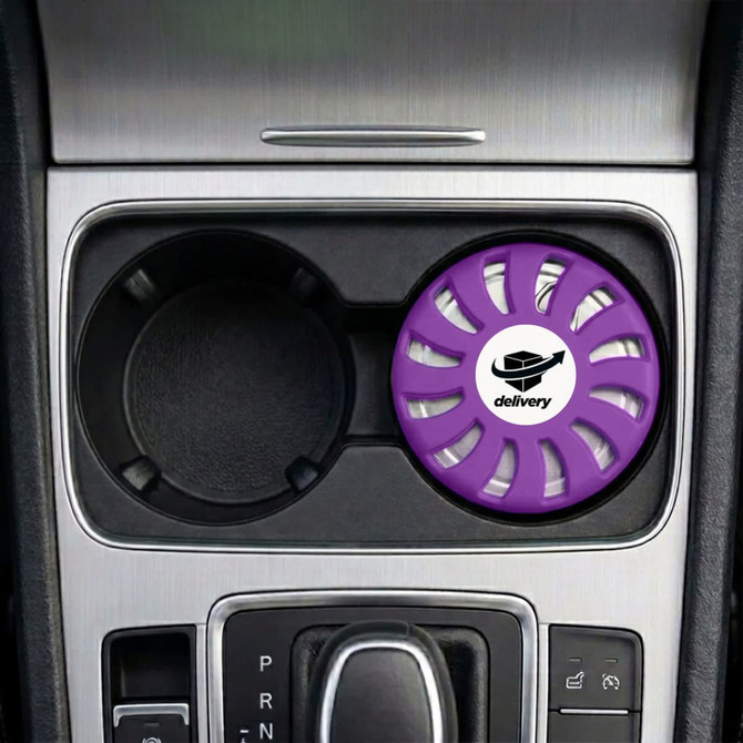 A round lavender air freshener sits in a car cup holder, featuring a logo in the centre.