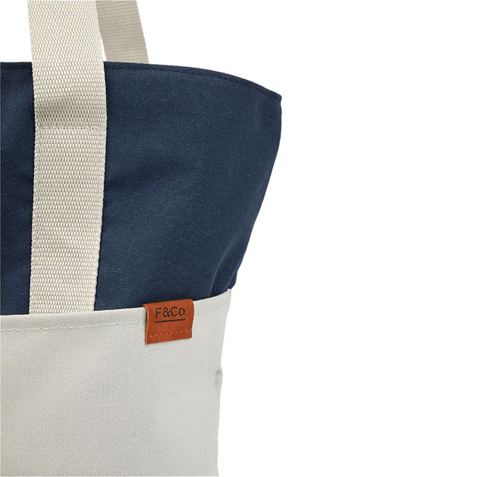 A tote bag featuring a navy blue top and a cream bottom, with a small logo tag.